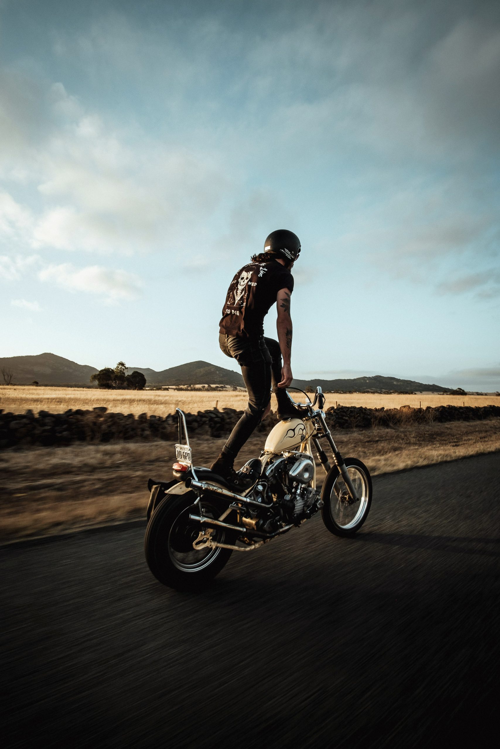 A Harley chopper rider in rural Australia stands upright on his bike as it travels down the road