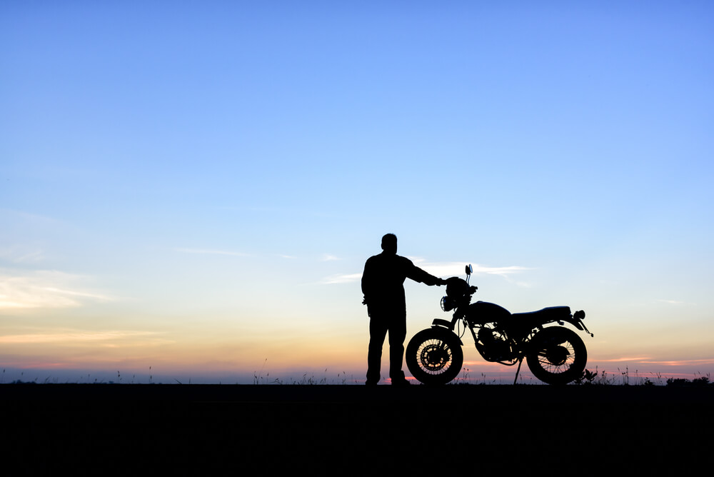 A view of a rider enjoying a sunset next to his motorcycle