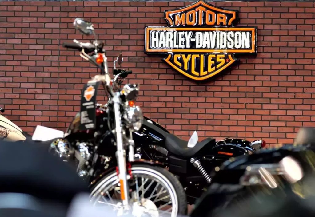 A Harley-Davidson logo with Harley bikes in front of it. Media sourced from ET Auto. 